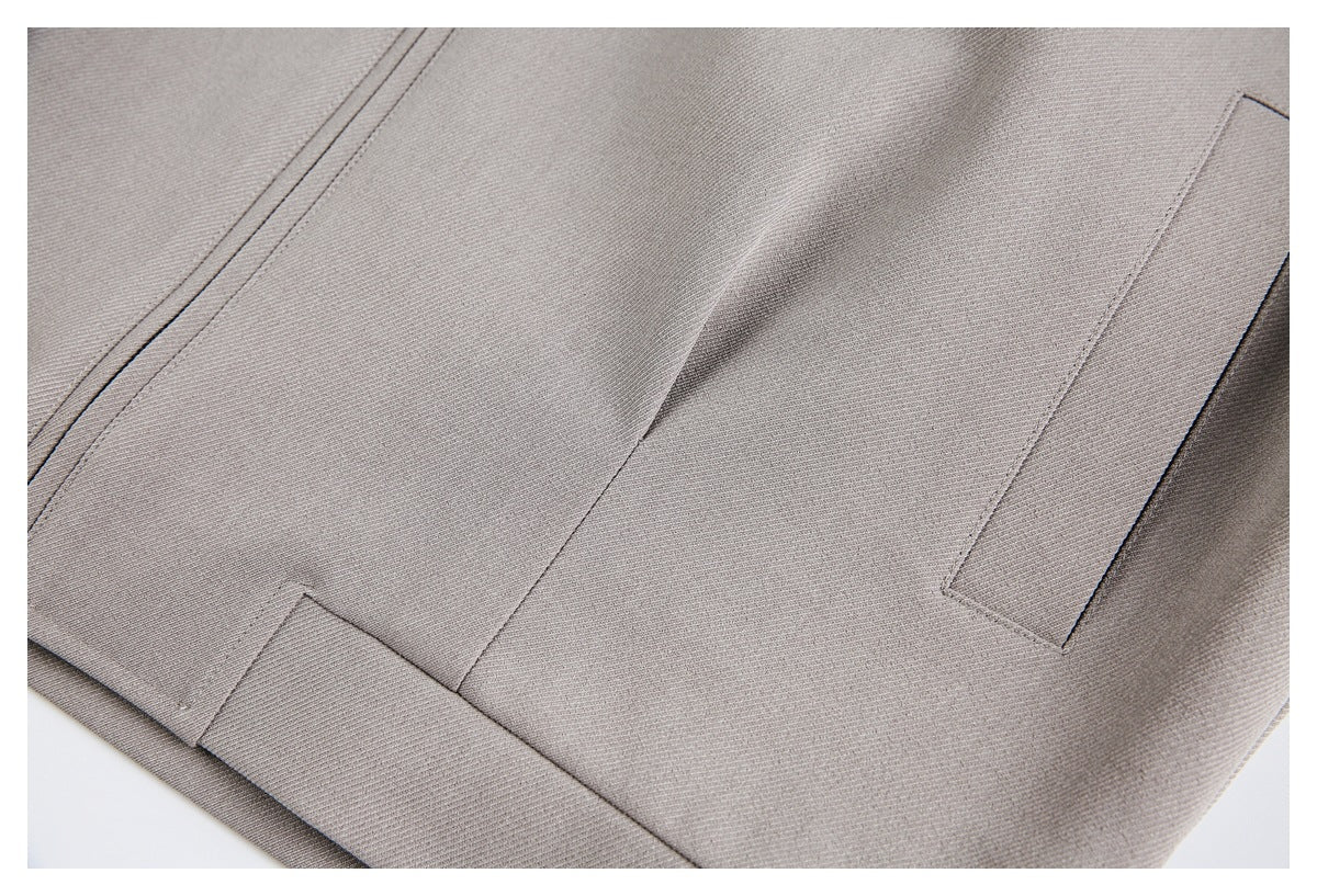 Close-up of taupe jacket seams, lower edge, and a narrow pocket opening.