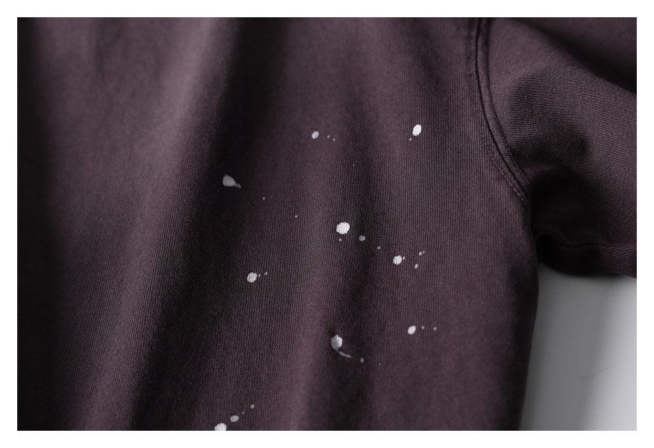 Close-up of scattered white paint-like spots on the front of a dark plum shirt.