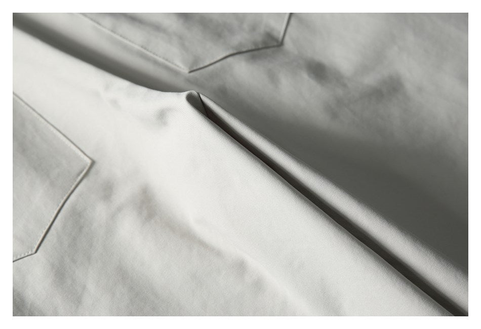 Close-up of a stitched pocket edge and folded fabric on light gray trousers.