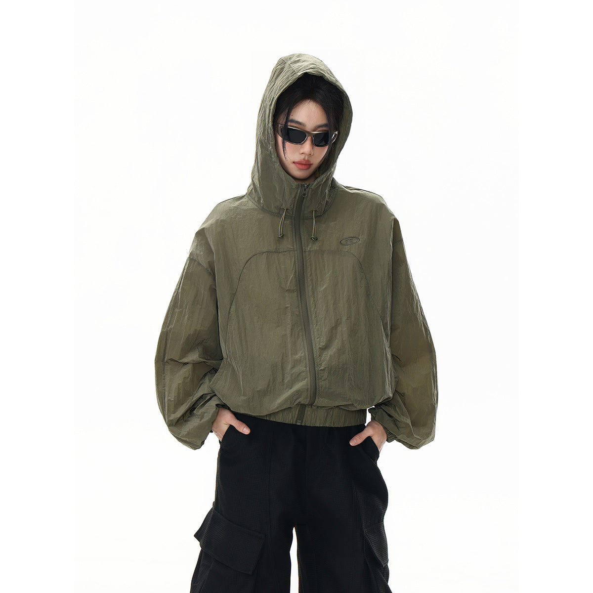 Model wearing an olive hooded zip jacket with a front emblem, shown from the front.