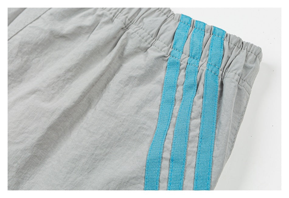 Close-up of three turquoise side stripes beside the elastic waistband on light gray shorts.