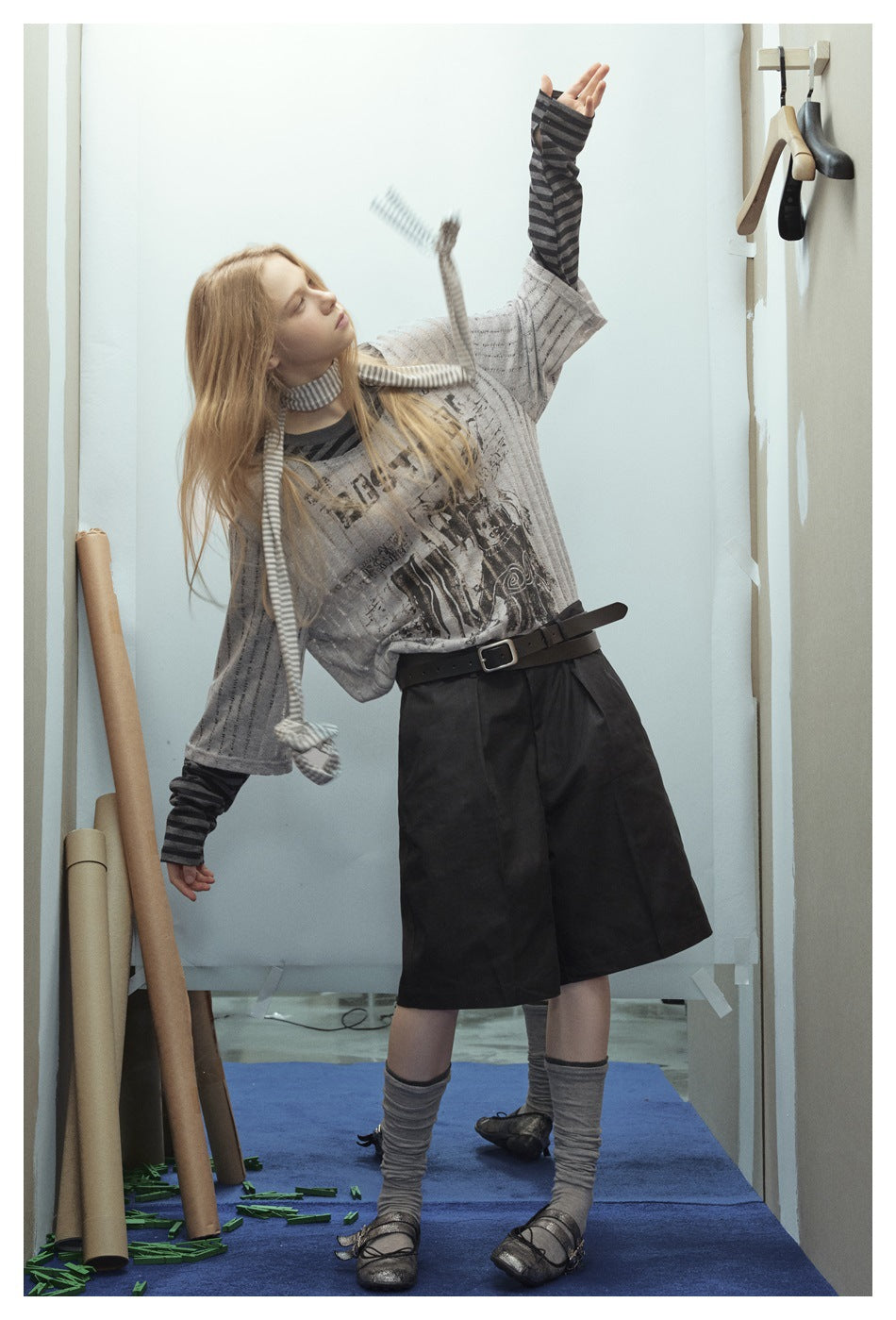 Model wearing a loose gray graphic T-shirt over a dark striped long-sleeve top, with black wide-leg shorts.
