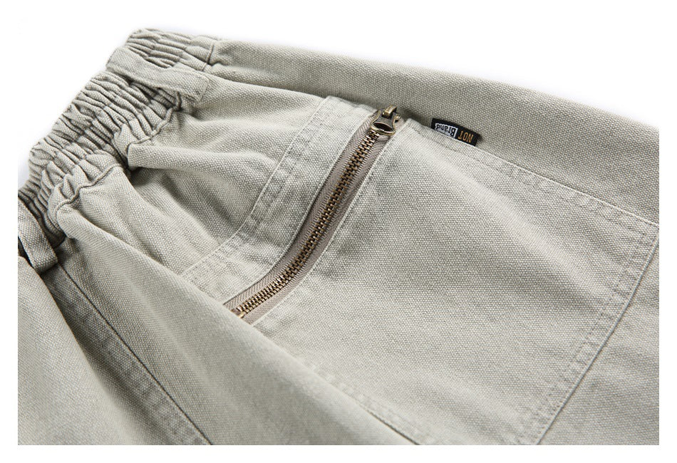 Close-up of light gray-beige trousers showing an elastic waistband, diagonal zip pocket, and small black label.