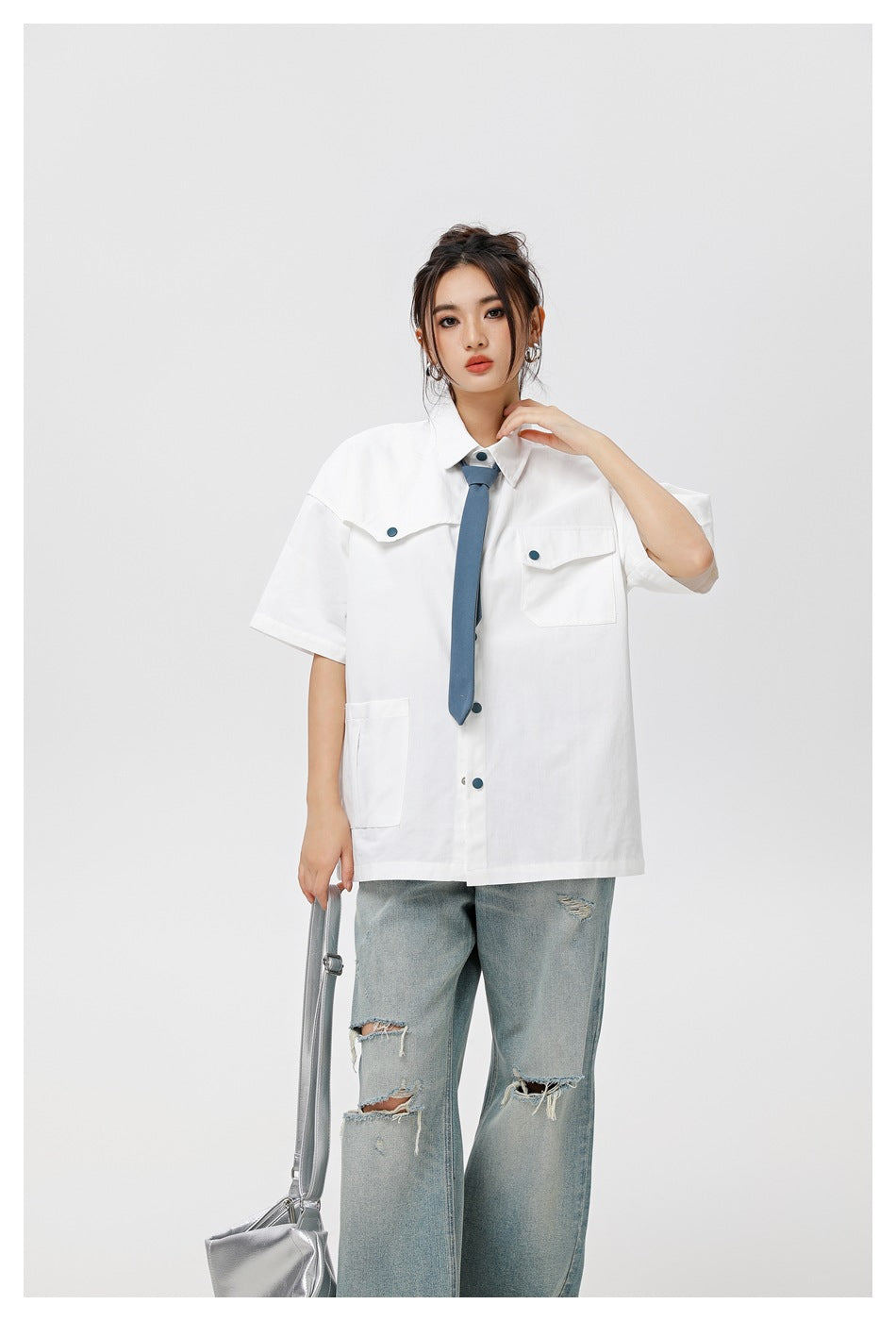 Closer view of a model wearing an oversized white shirt with flap pockets and a blue tie.