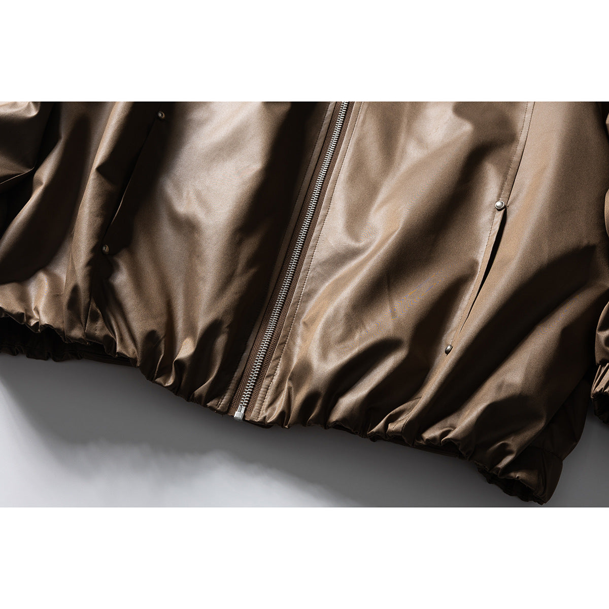 Close-up of the jacket's lower front, showing the center zipper, snap pockets, and gathered hem.