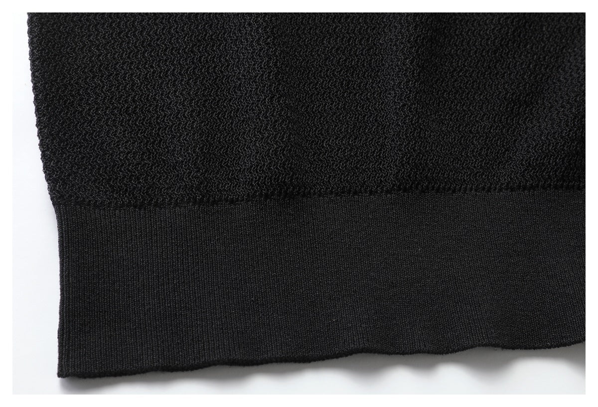 Close-up of a black knit garment showing textured fabric above a smooth ribbed hem.