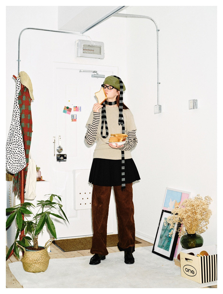 Model wearing a beige short-sleeve top over striped sleeves, black skirt, brown trousers, green beret and long striped scarf.