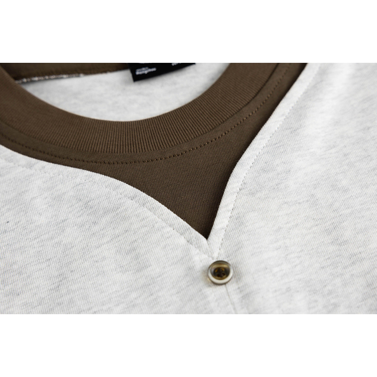 Extreme close-up of the shirt's dark brown ribbed collar, V-shaped front opening, and button.