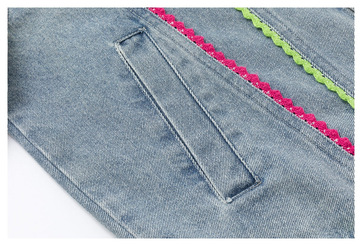 Close-up of a denim jacket pocket and stitched seams beside diagonal pink and lime scalloped trim.