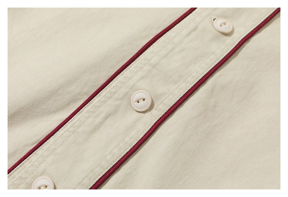 Close-up of an ivory garment's button placket with burgundy piping and cream buttons.