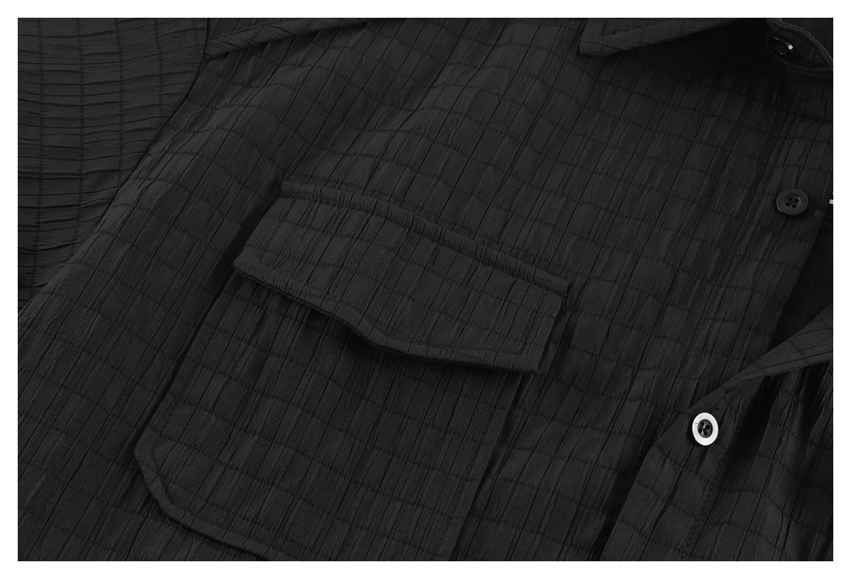 Close-up of a black shirt's flap chest pocket and button placket against a subtle grid texture.