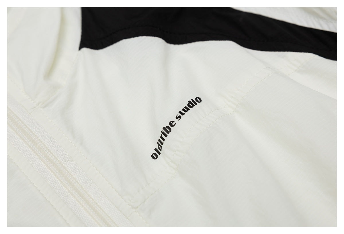 Close-up of a white garment with a zipper and black trim; the fabric is printed with “oldtribe studio.”