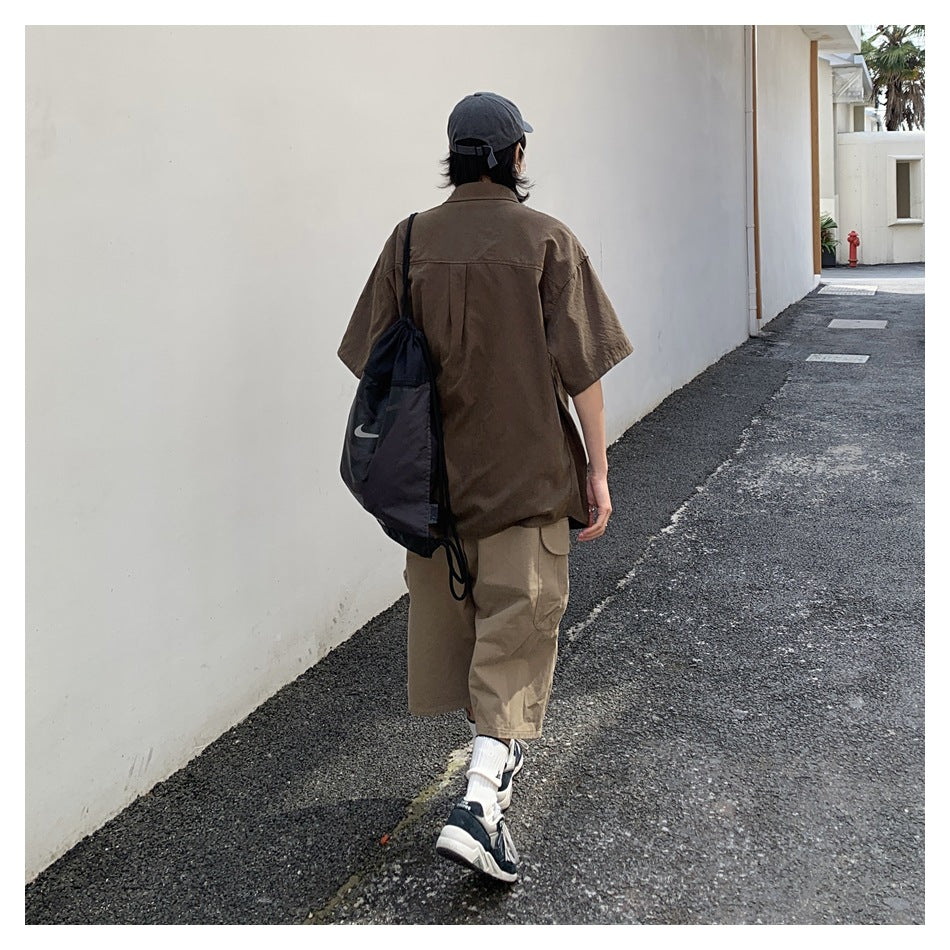 Rear view of a person wearing an oversized brown short-sleeve shirt and loose khaki pants outdoors.