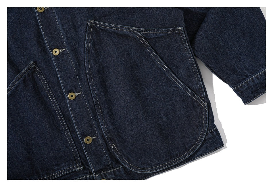 Close-up of the dark denim jacket's front with large curved patch pockets, tan buttons, and contrast stitching.