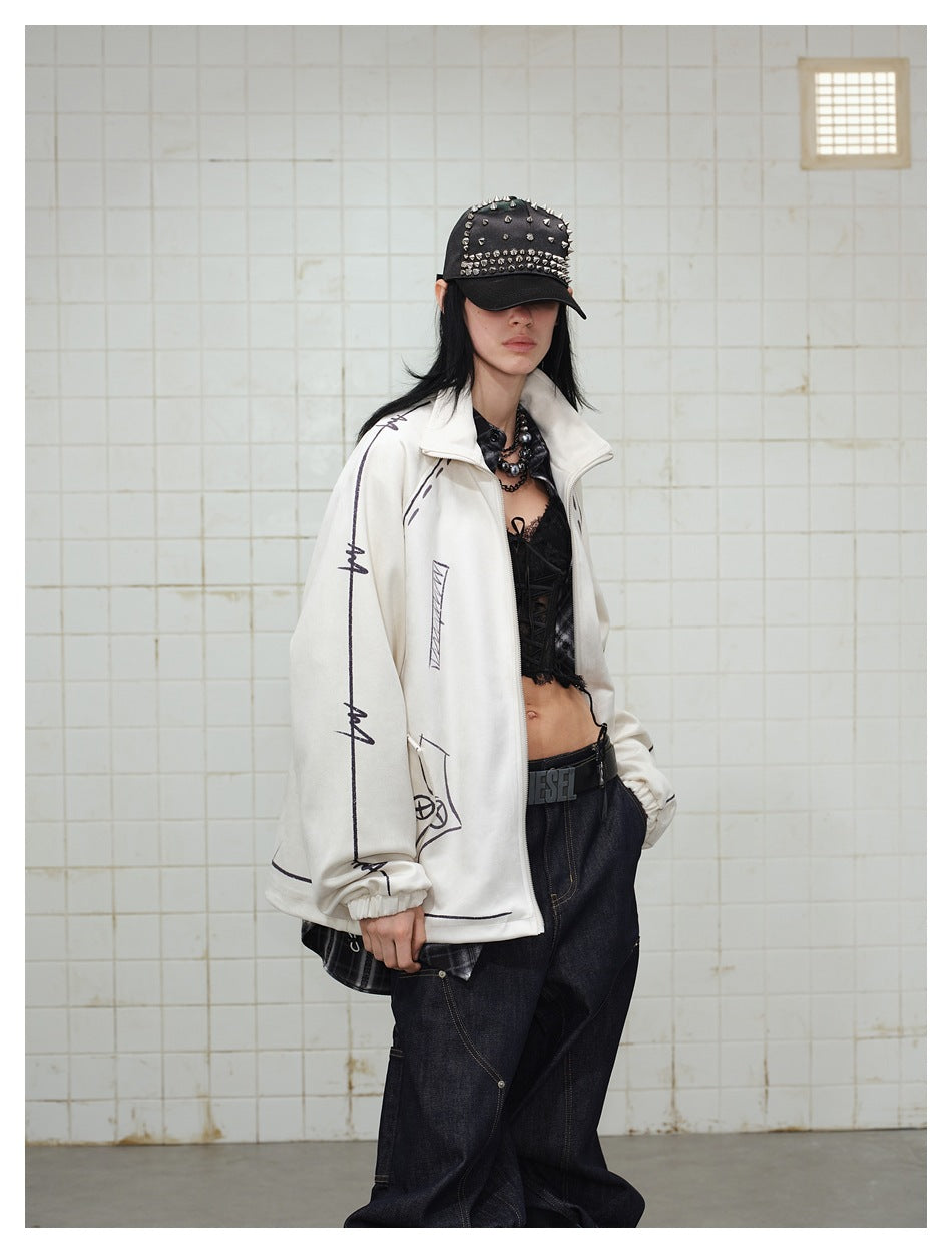 Closer view of a model wearing the cream graphic zip jacket over black layers with dark jeans and a studded cap.