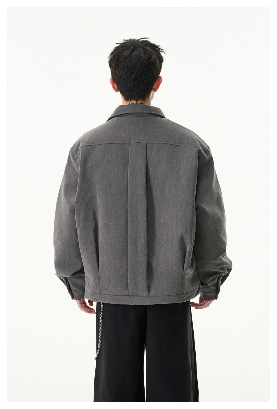 Rear view of a model wearing a charcoal gray jacket with a center back pleat and buttoned cuffs.