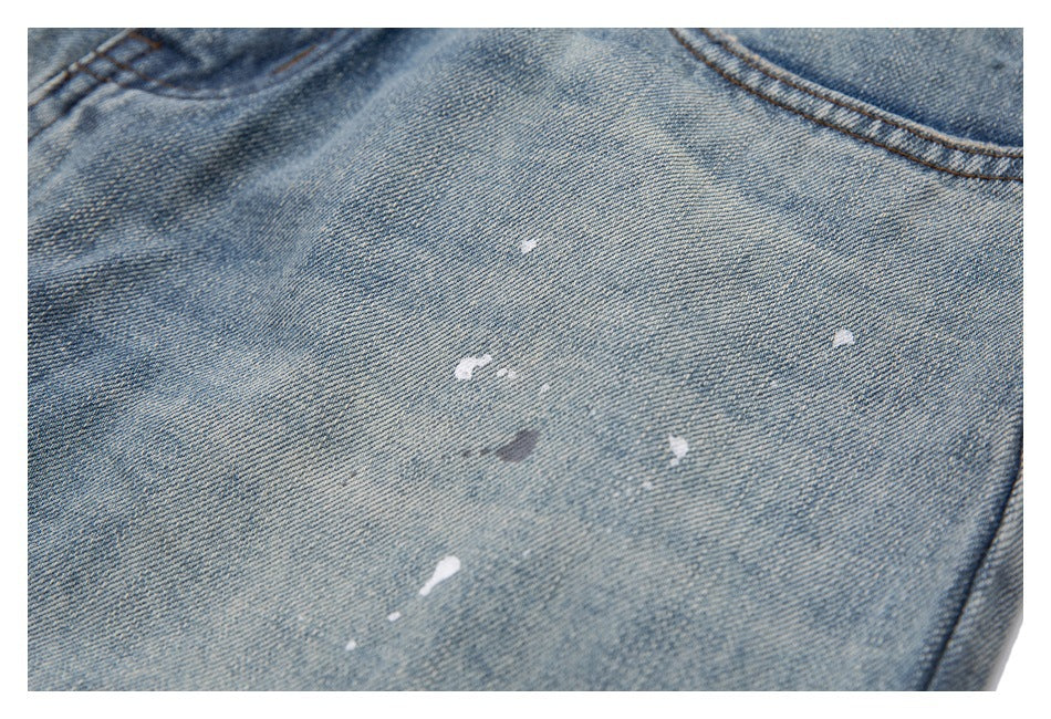 Close-up of light blue denim with scattered paint splatters and a stitched seam.