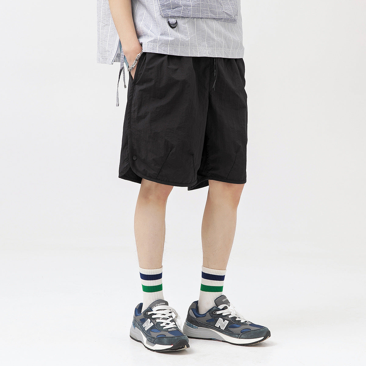 Model wearing loose black shorts with a drawstring waist and side snaps, shown at an angle.