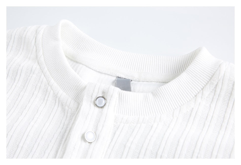 Close-up of a white ribbed shirt's crew neckline and two snap buttons.