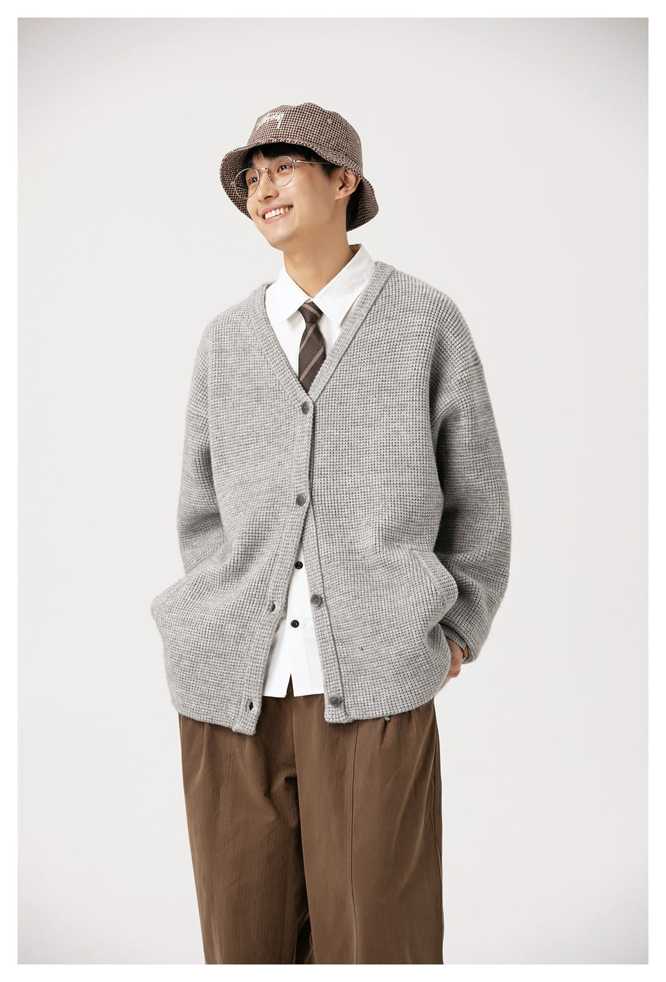 Model wearing a light gray button-front V-neck cardigan with front pockets, brown trousers, and a white shirt.