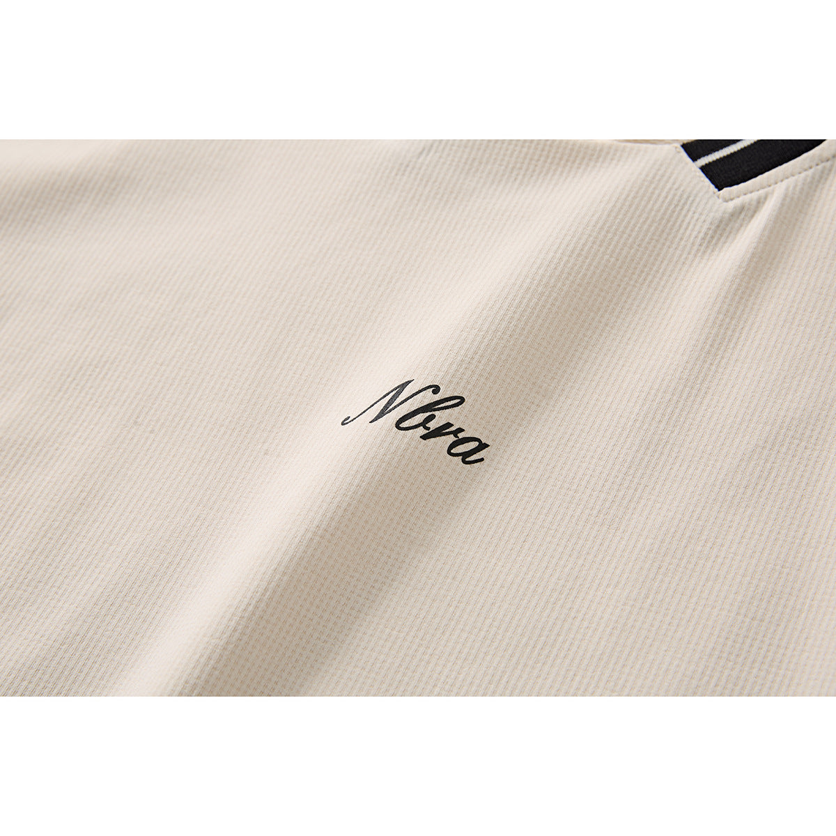 Close-up of an ivory shirt showing a small black cursive chest logo and a glimpse of striped neckline trim.