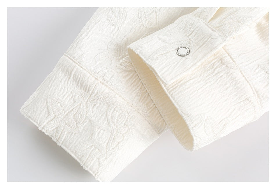 Close-up of a white fabric cuff with a small silver-tone ring button and raised floral pattern.