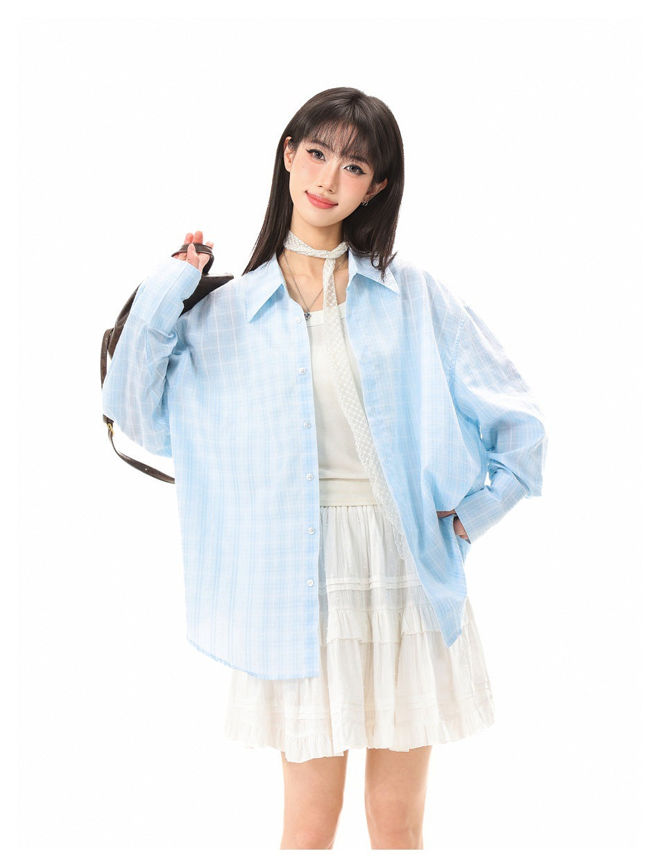 Model posing in an open light-blue plaid shirt over a white top and ruffled skirt.