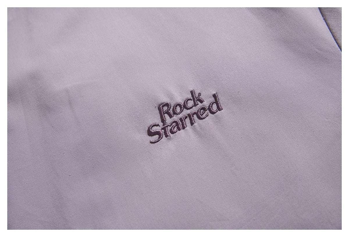 Close-up of dark embroidered “Rock Starred” lettering on lavender fabric.