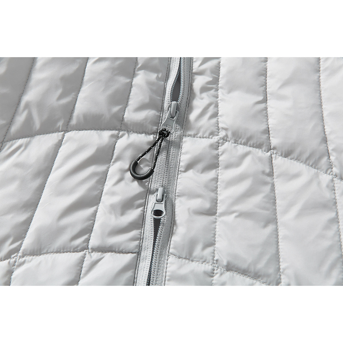 Close-up of the light gray jacket’s center zipper, two sliders, and black pull cord against quilted panels.