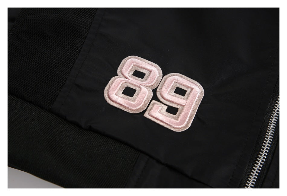 Black jacket detail with a pale pink embroidered 89, black mesh panel, ribbed trim, and silver zipper.