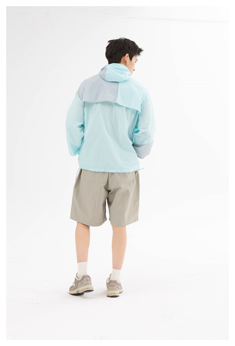 Back view of a model wearing a pale aqua hooded jacket and taupe shorts, shown full length.
