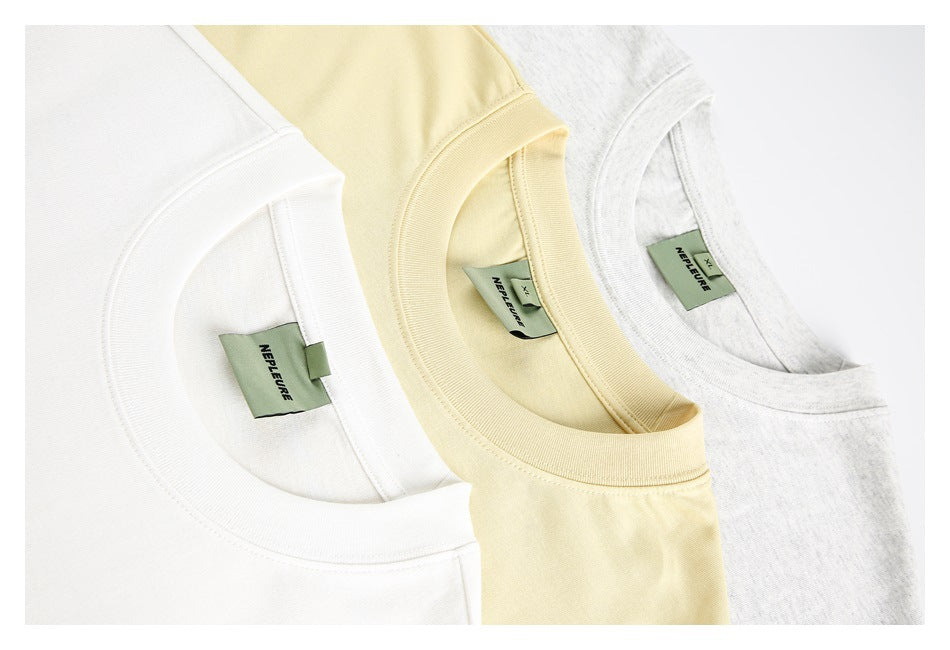 Close-up of three T-shirt collars in white, pale yellow, and light gray, each with a green neck label.