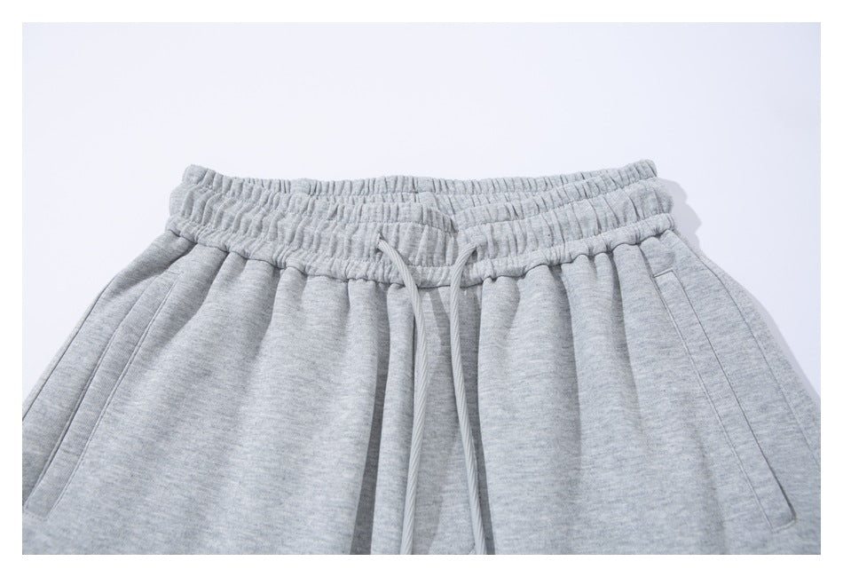 Close-up of the gathered waistband, drawstring, and slanted pockets on light gray sweatpants.