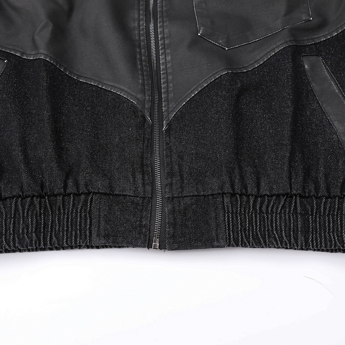 Close-up of the black jacket's lower front, showing its zipper, pockets, contrasting panels, and elastic hem.