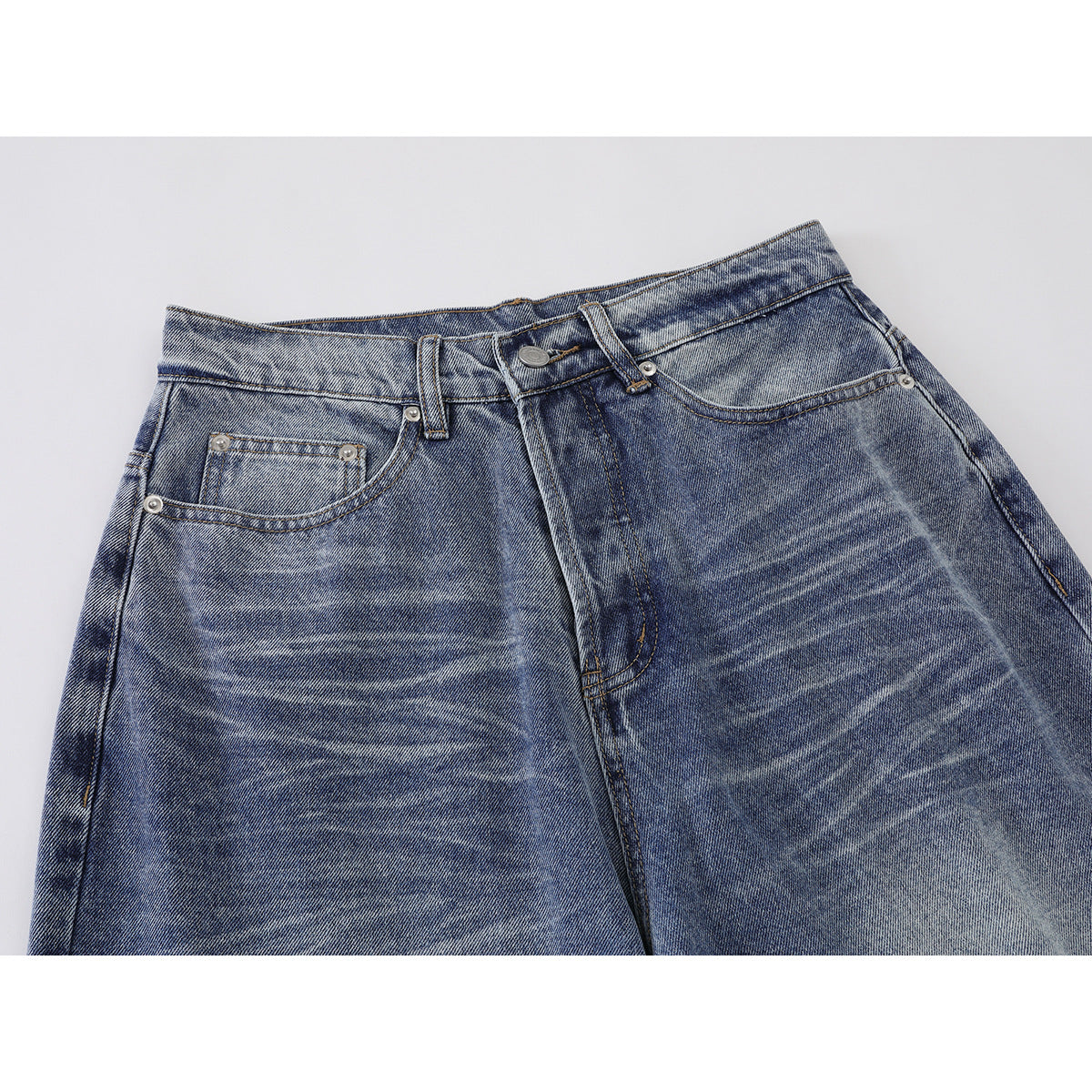 Close-up of blue washed jeans showing the waistband, button, fly, belt loops, and front pockets.