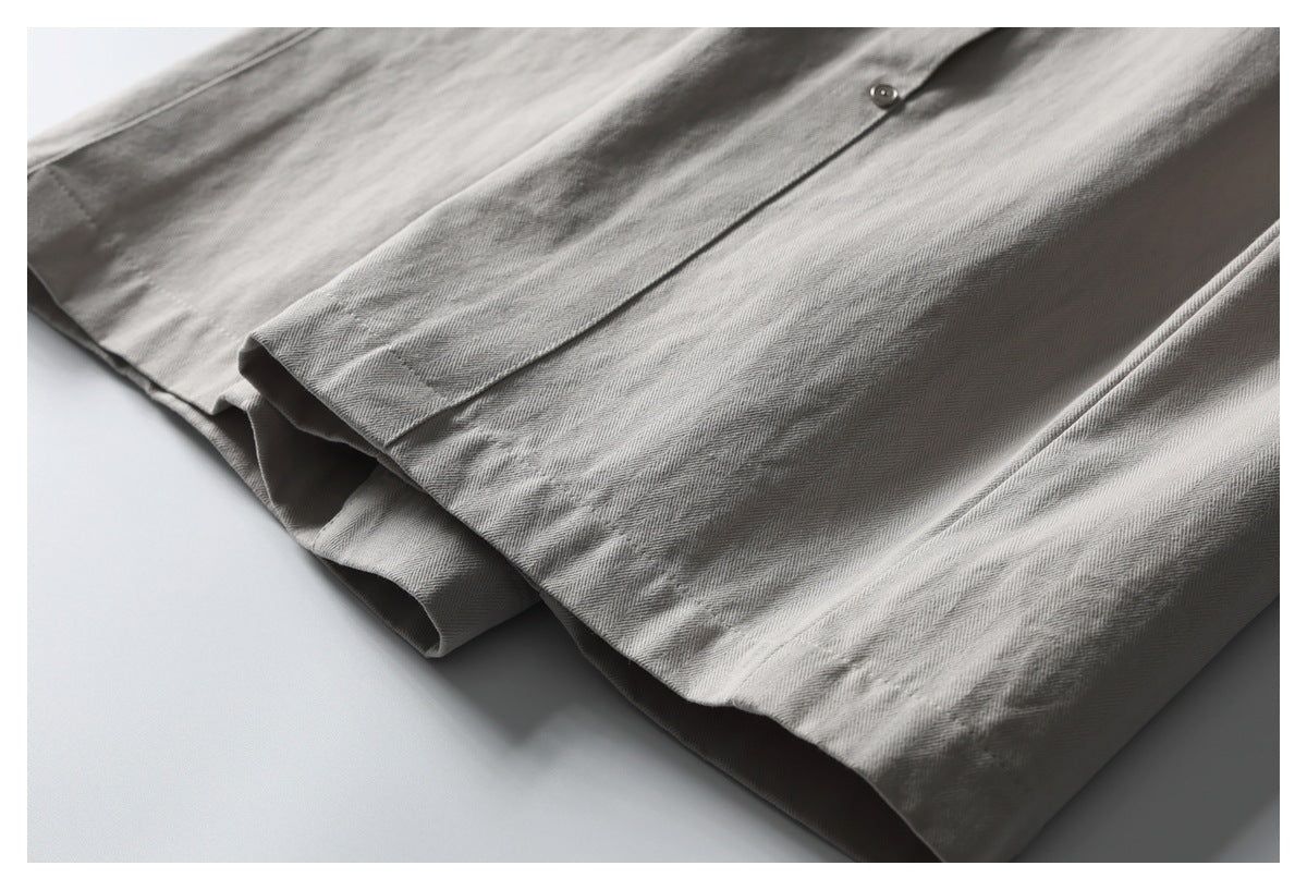 Close-up of light gray-beige garment fabric with a small button and folded hem.