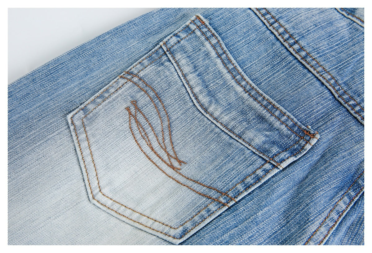 Close-up of a back pocket on faded blue jeans with decorative brown stitching.