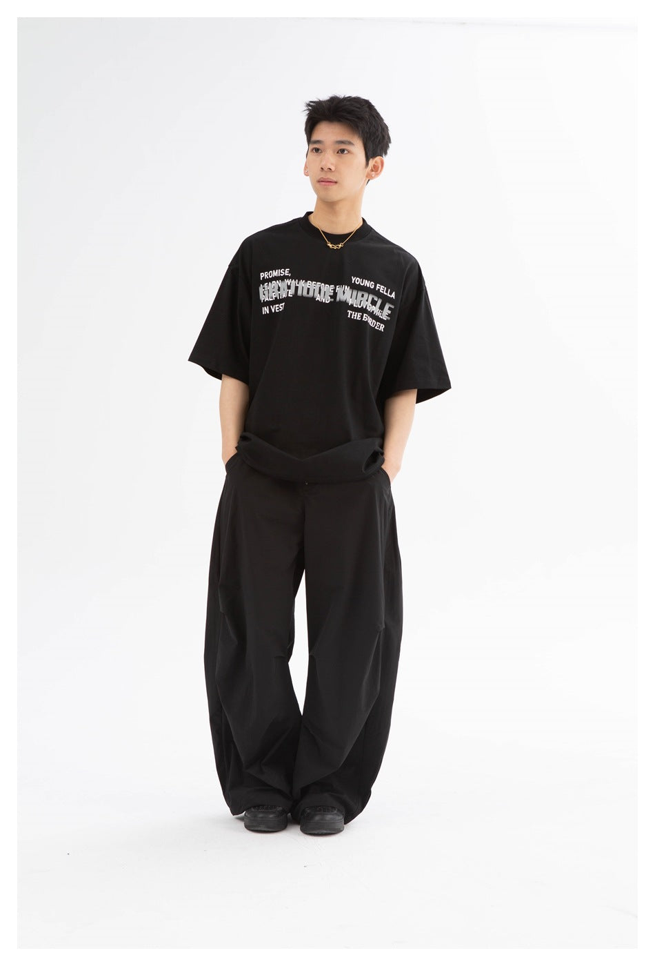 Model wearing a black oversized graphic t-shirt with black wide-leg pants, front view, hands in pockets