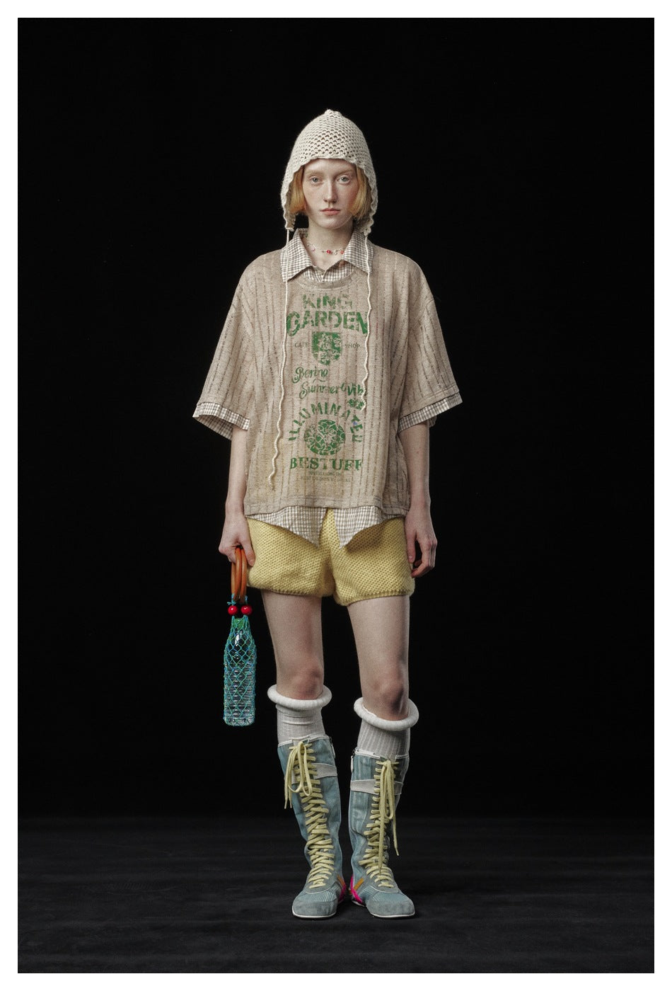 Model wearing the brown plaid-trimmed striped top with green graphic, yellow shorts, knit hat and lace-up boots