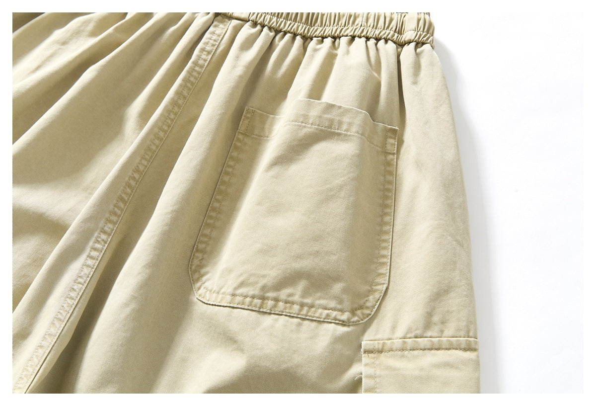 Close-up of beige shorts showing the gathered elastic waistband, large patch pocket, and stitched seams.
