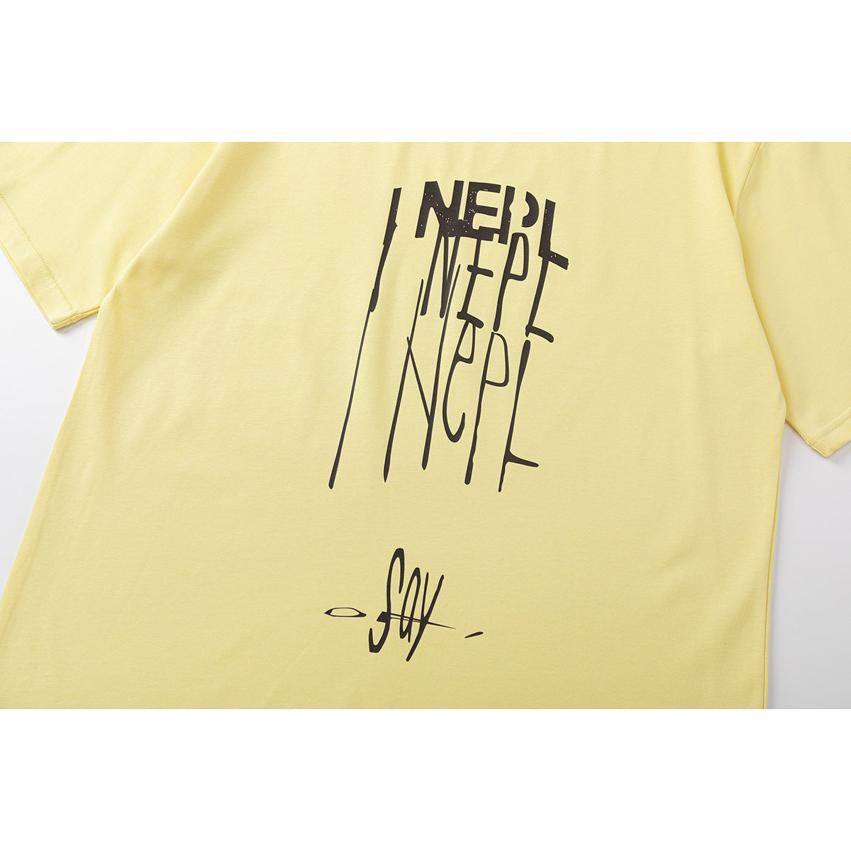 Close-up of a pale yellow T-shirt front with tall black stylized lettering and a small script graphic.
