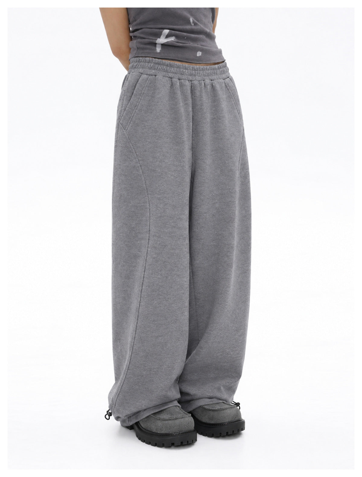 Person wearing gray wide-leg sweatpants with a gray top and chunky shoes, showing curved seams and hem toggles