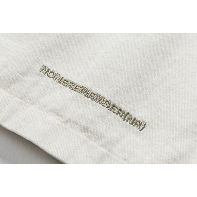 Close-up of small metallic-looking embroidered lettering on the hem of an off-white garment.