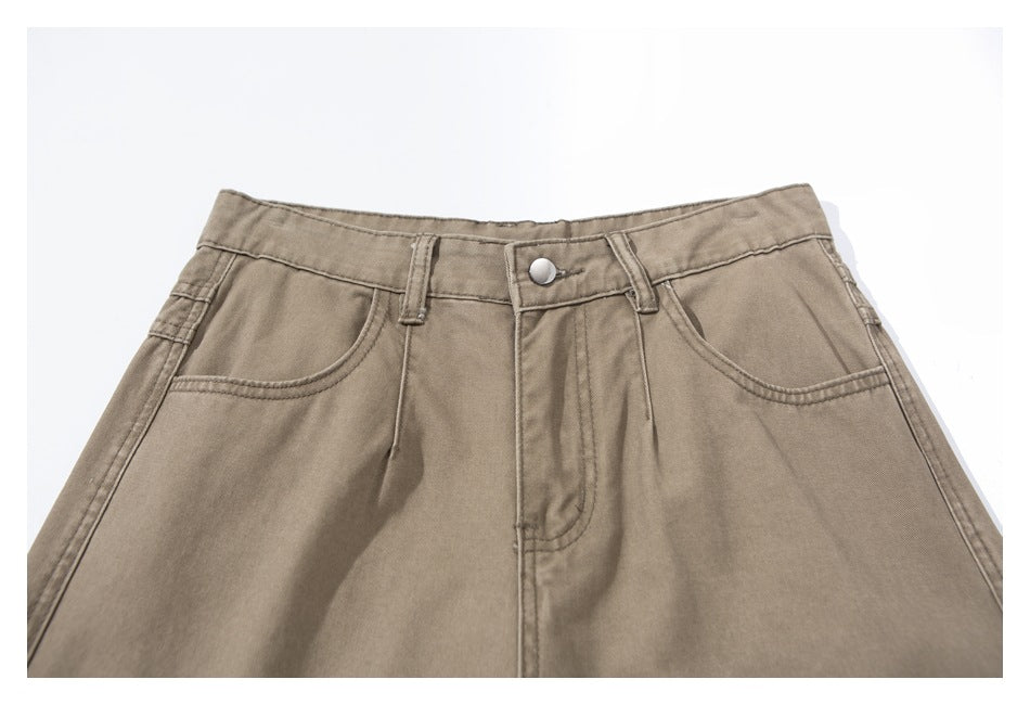 Close-up of taupe pants showing the front waistband, metal button, belt loops, fly, and curved pockets.