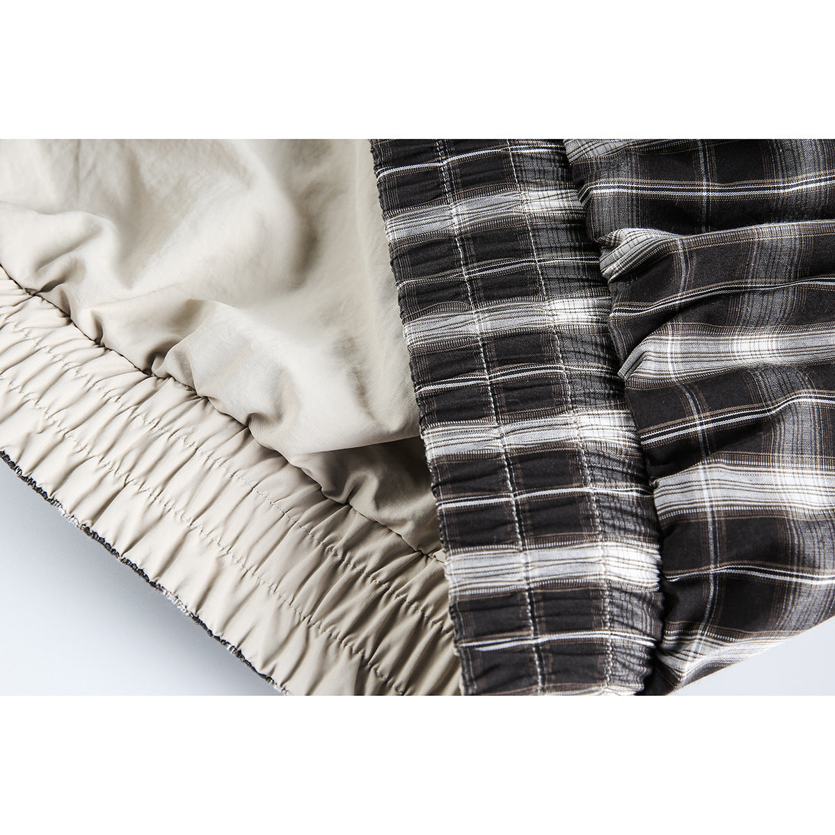 Close-up of the jacket's gathered cream lining beside black-and-white plaid fabric and a stitched seam.