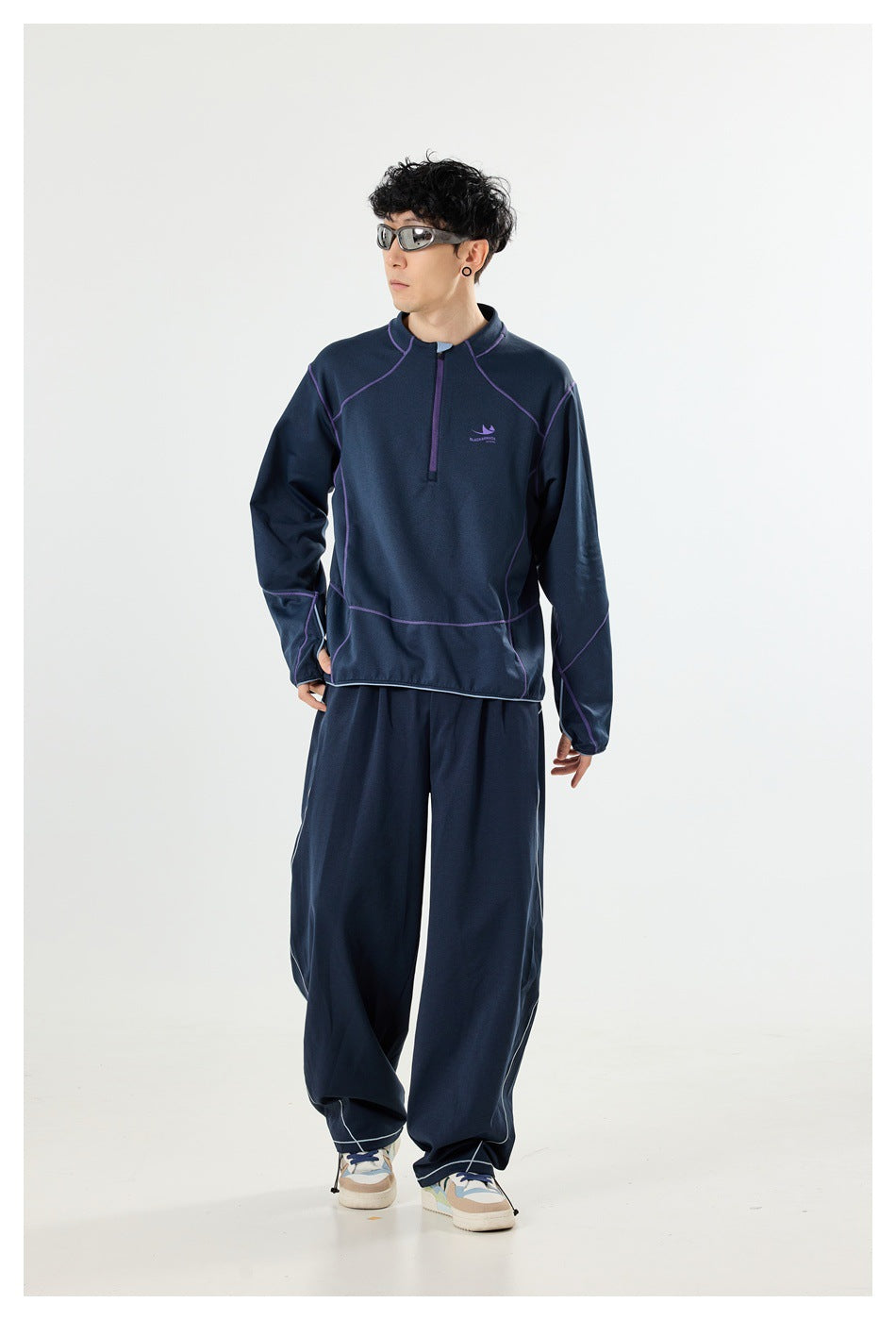 Model wearing a navy quarter-zip pullover with purple seam detailing and matching wide-leg trousers.