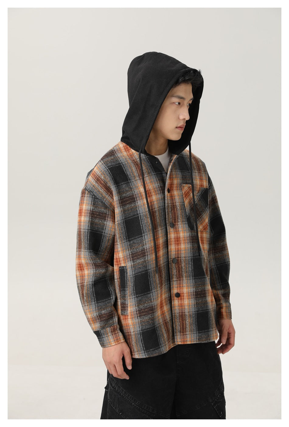 Man wearing a gray, black, and rust plaid hooded shirt jacket with the hood up, shown from the front at an angle.