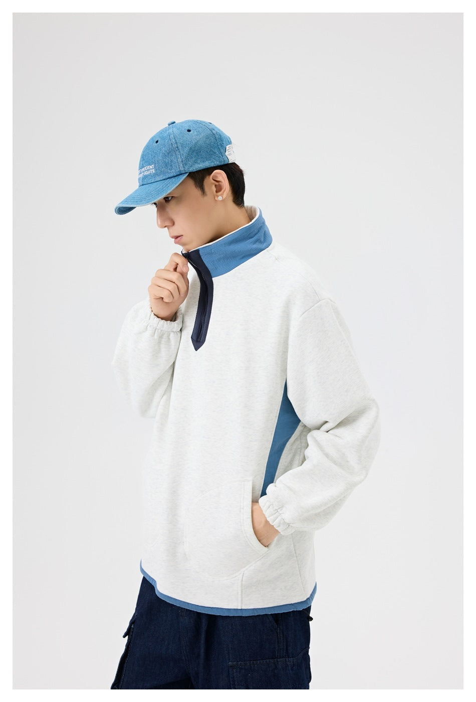 Man modeling a light gray pullover with a blue stand collar and side panel, navy quarter zip, and kangaroo pocket.