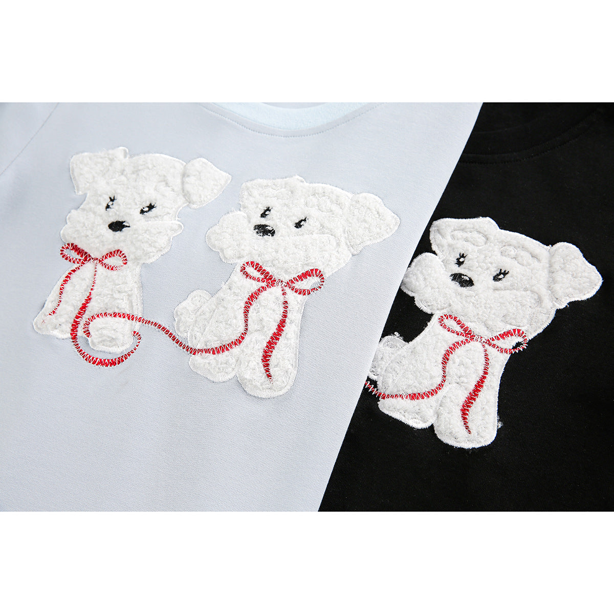 Close-up of white teddy bear appliqués with red stitched details on pale blue and black T-shirts.