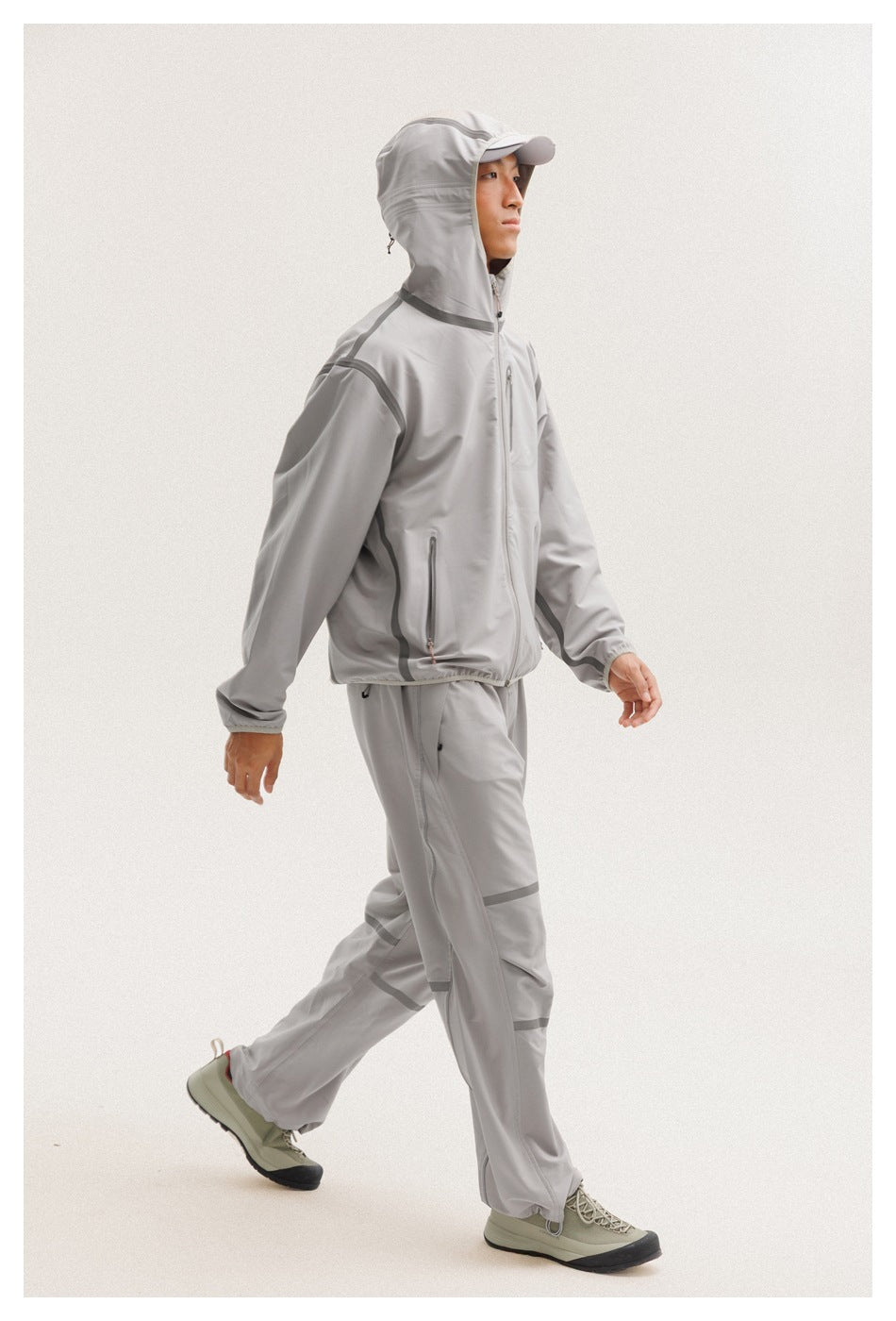 Model walking in a light gray hooded jacket with matching pants and dark seam accents.
